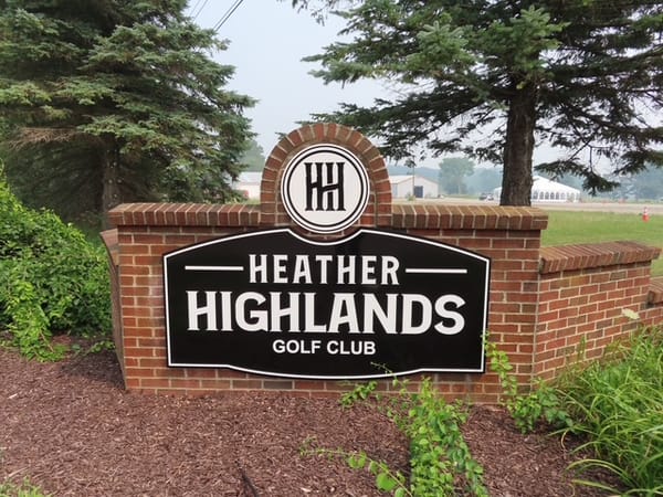 The brick entrance sign at the road: a black board reading Heather Highlands Golf Club beneath the HH monogram